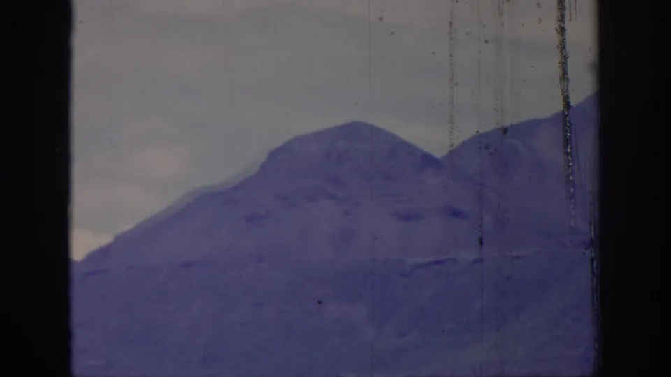 1966 8mm view of a broad mountain slope seen through a dark frame division, with visible film wear and purple aging.