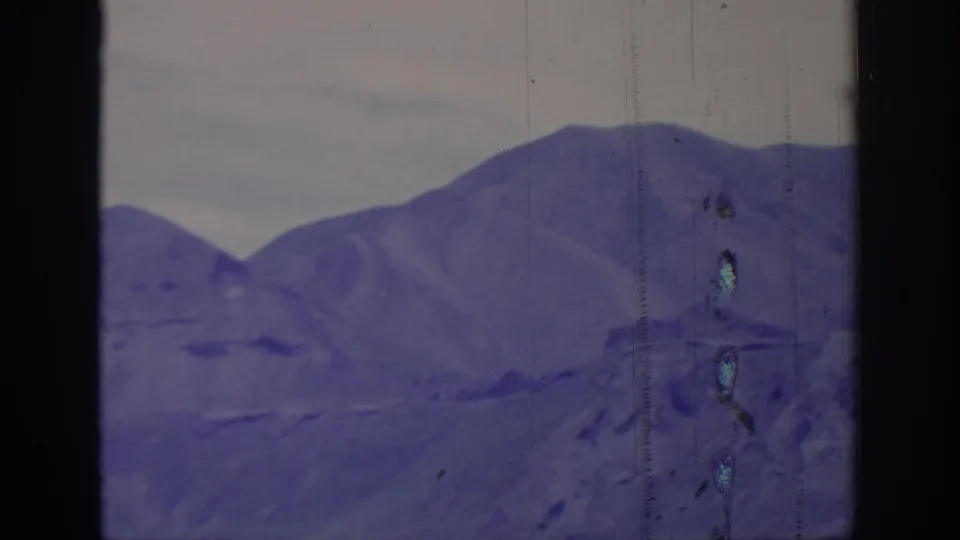 1966 8mm frame of layered mountain ridges viewed through dark framing, with soft focus, scratches, and faded color.