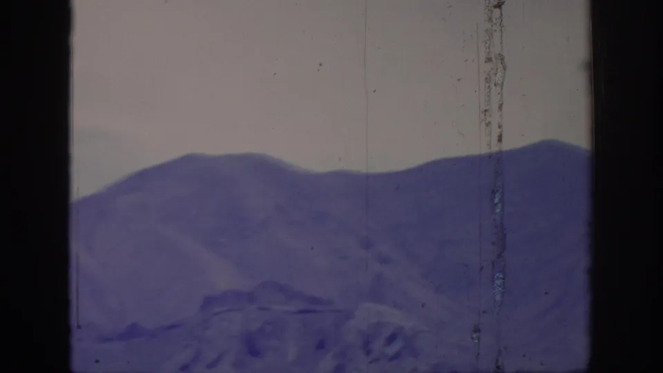 1966 8mm frame showing a lower mountain ridge beneath a pale overcast sky, bordered by dark frame edges and film wear.