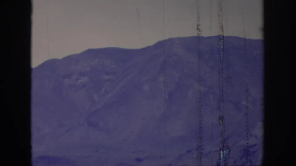 1966 8mm frame labeled Sacramento, California, showing a rocky purple mountain slope beneath pale sky with visible scratches and aged-film texture.