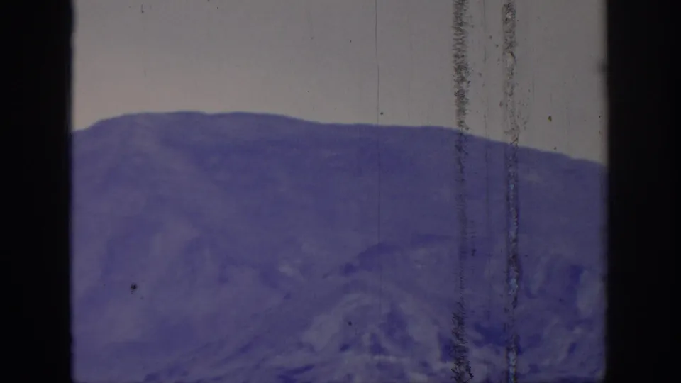 1966 8mm home-movie frame labeled Sacramento, California, showing a broad purple mountain slope with pale sky and heavy vertical film wear.