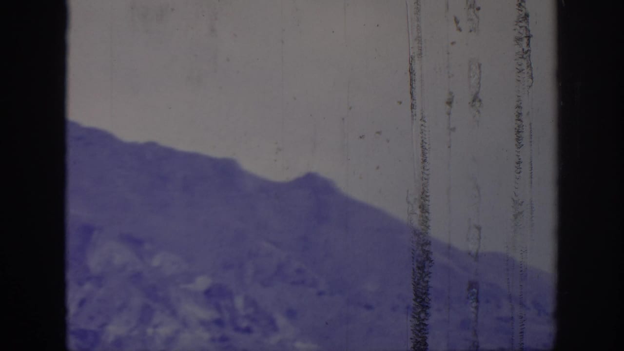 Rocky mountain slope beneath a clear sky, divided by dark vertical film edges and surface wear.