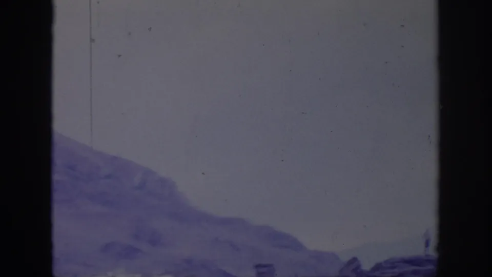 1966 8mm landscape frame showing a rocky treeless ridge fading rightward beneath a pale sky, with visible gate edges and scratches.