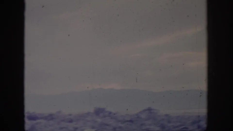 1966 Sacramento-area 8mm frame with rocky foreground, muted water, distant hills, and overcast sky in faded color.
