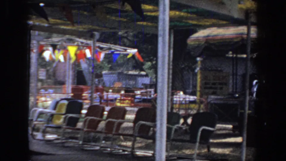 1966 Sacramento carnival pan showing empty chairs, colorful pennants, striped umbrellas, metal railings, and a shaded concession area.