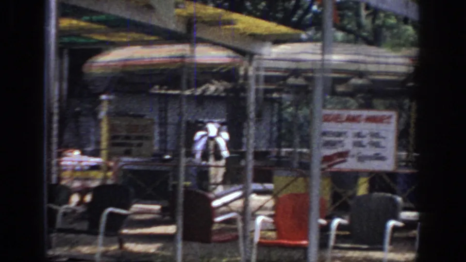 1966 Sacramento carnival frame with concession umbrellas, scattered chairs, trees, fencing, and a partially readable sign in the fairground.