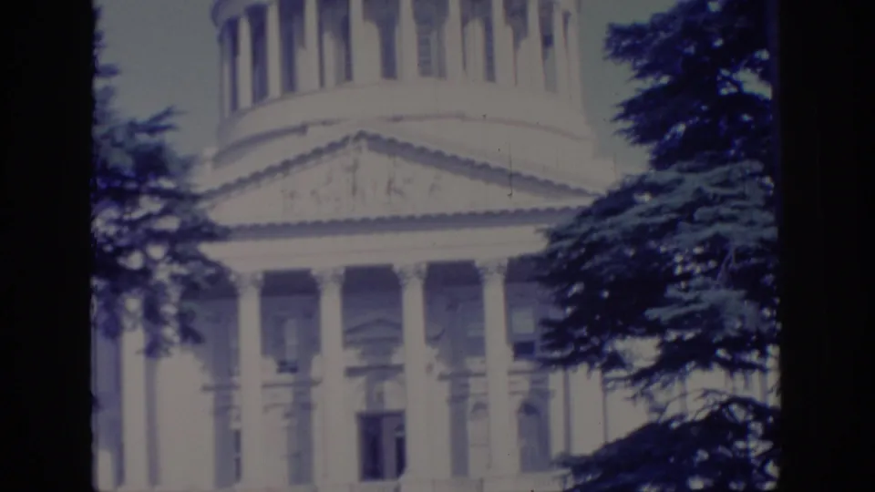 1966 Sacramento view tilting up toward the California State Capitol dome base and columned facade through trees.