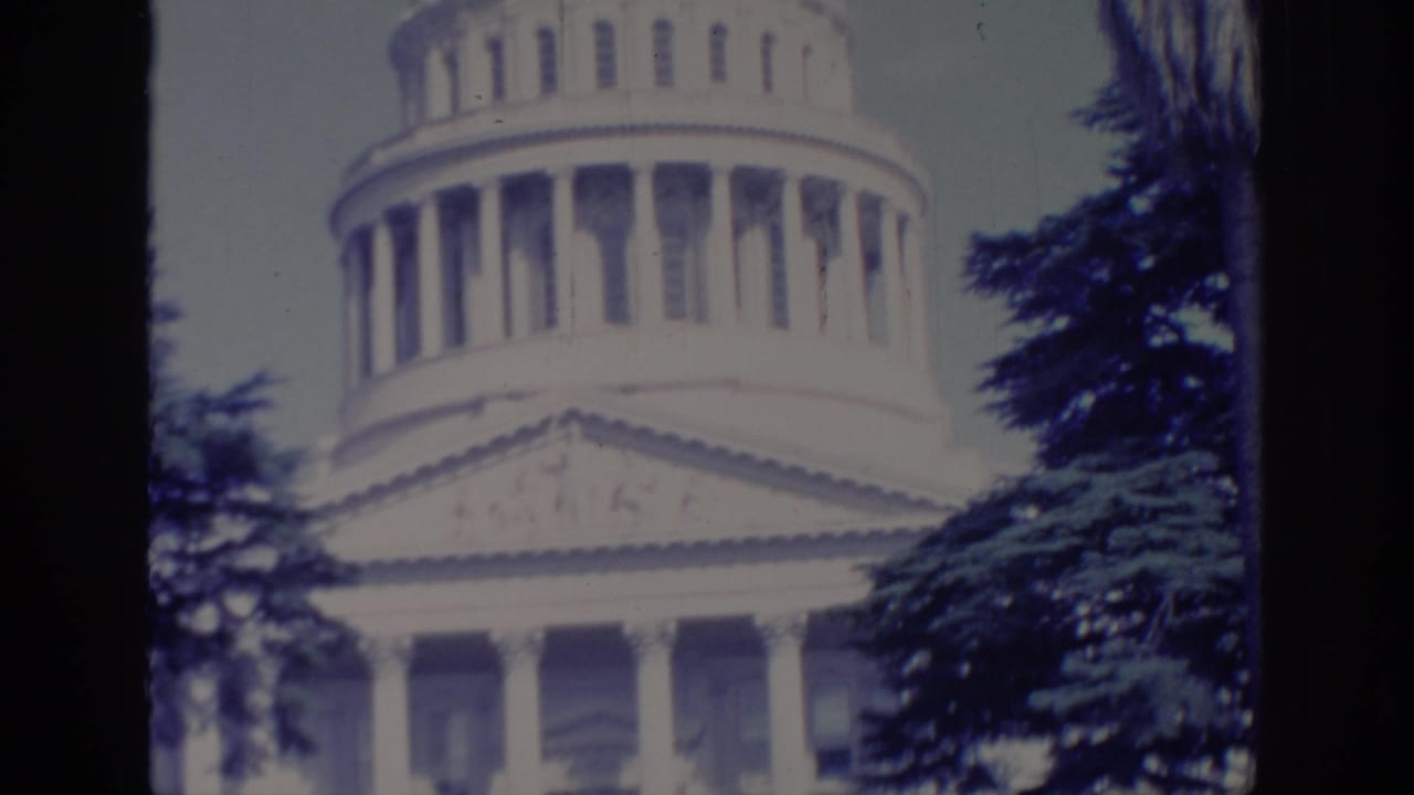 Sacramento Capitol exterior in 1966, showing the white dome, columns, and tree branches in a soft 8mm frame.