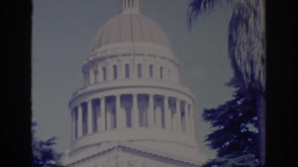 1966 Sacramento Capitol shot with the dome, colonnade, evergreen branches, and palm frond visible in faded 8mm color.
