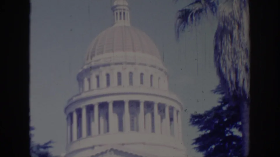 1966 Sacramento home-movie frame showing the California State Capitol dome and columns framed by palm trees and pale sky.