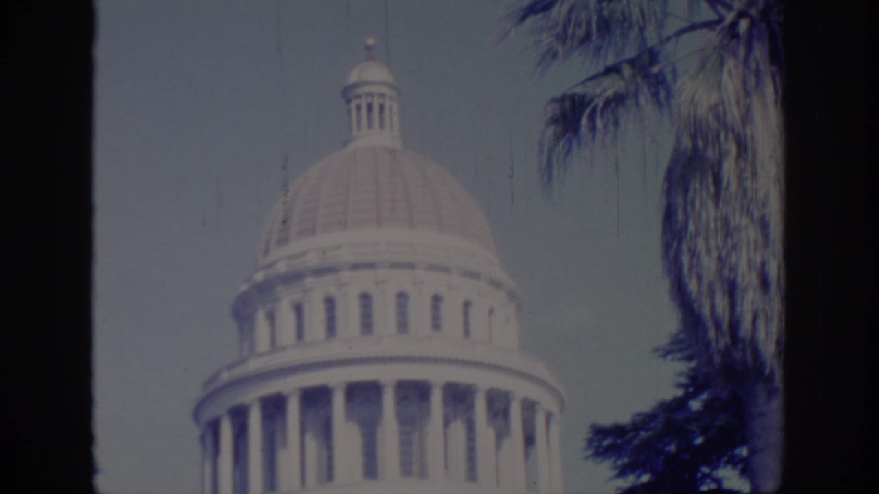 Domed Capitol building seen through dark film-frame edges with palm trees nearby.