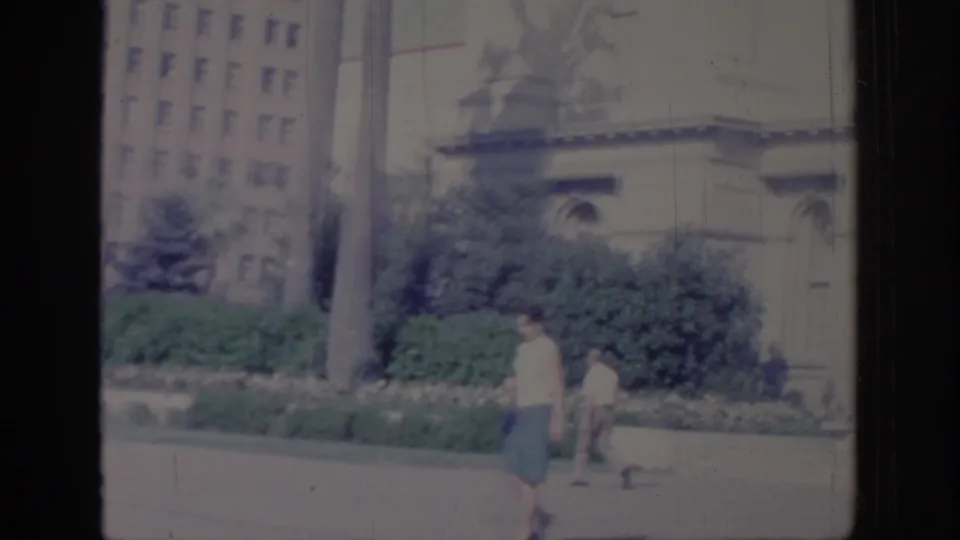 1966 Sacramento view of the Capitol grounds, showing the dome, facade, landscaped shrubs, walkway, and visitors in the distance.