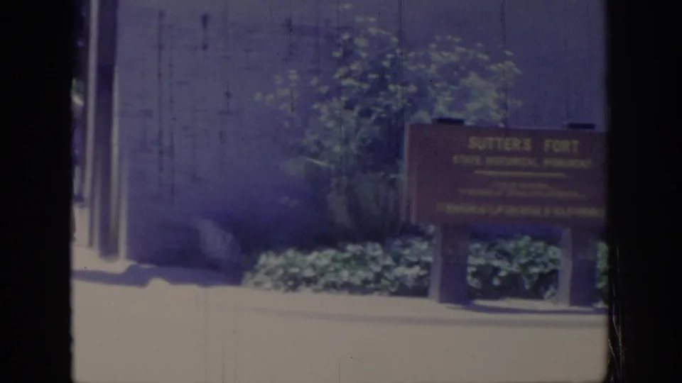 1966 Sacramento frame showing a Sutter's Fort State Historical Park sign near landscaping, a light wall, and possible people in the background.