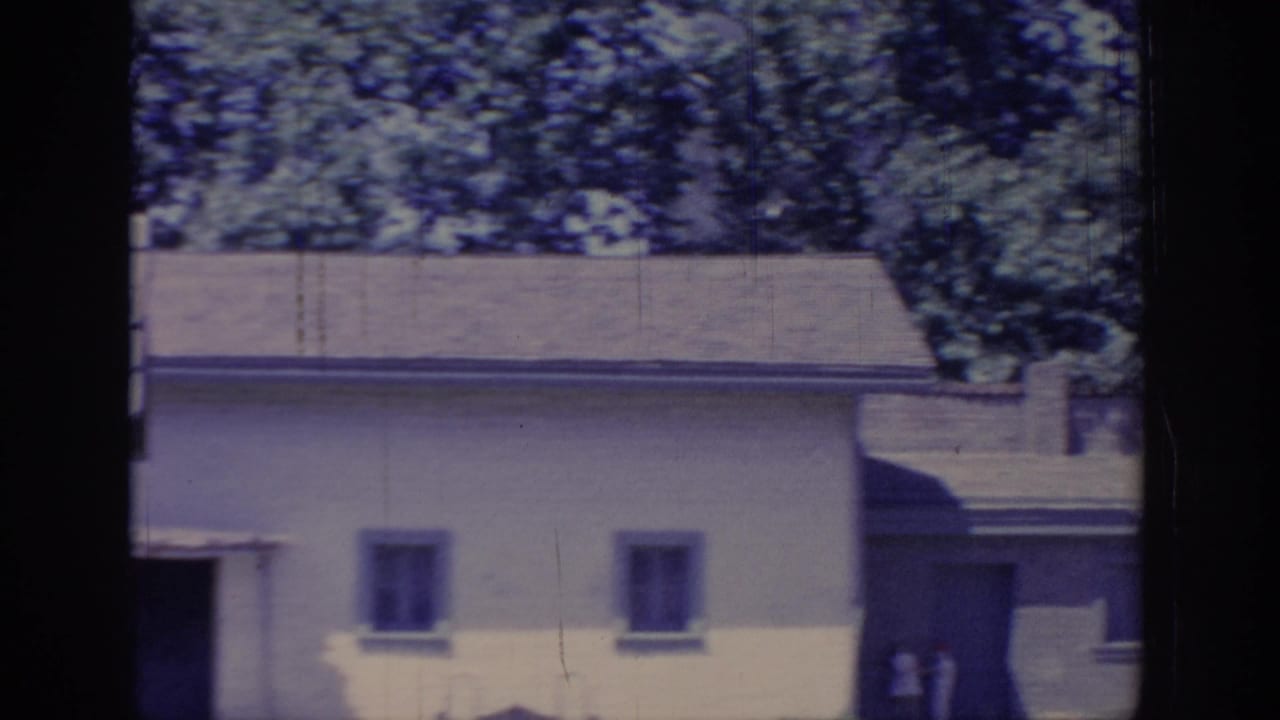 1966 Sacramento 8mm frame showing a yellow cottage wall, small windows, surrounding trees, and visible film gate shadows.
