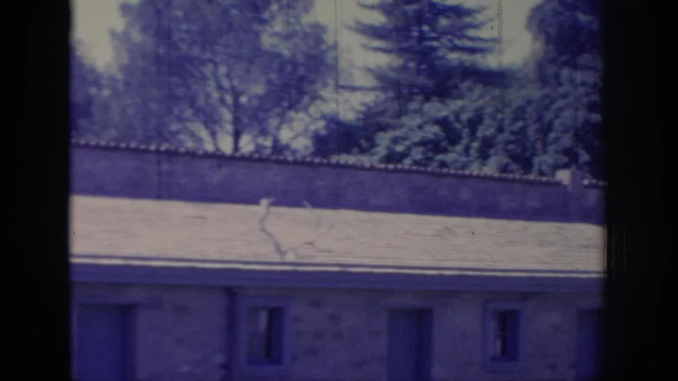 1966 Sacramento home-movie frame showing a tiled roof, walled garden, trees, and small lower windows with aged 8mm color shift.