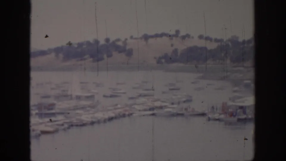 1966 Sacramento-area 8mm frame showing a marina with small boats, calm water, distant hills, and dark window-frame borders.