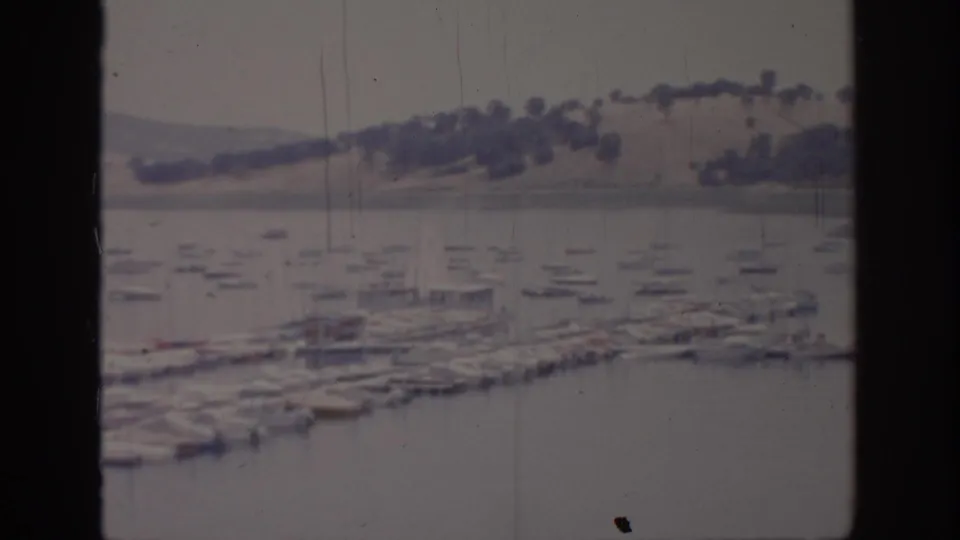 1966 Sacramento-area marina scene with rows of small boats, dock structures, calm water, and low tree-dotted hills beyond.