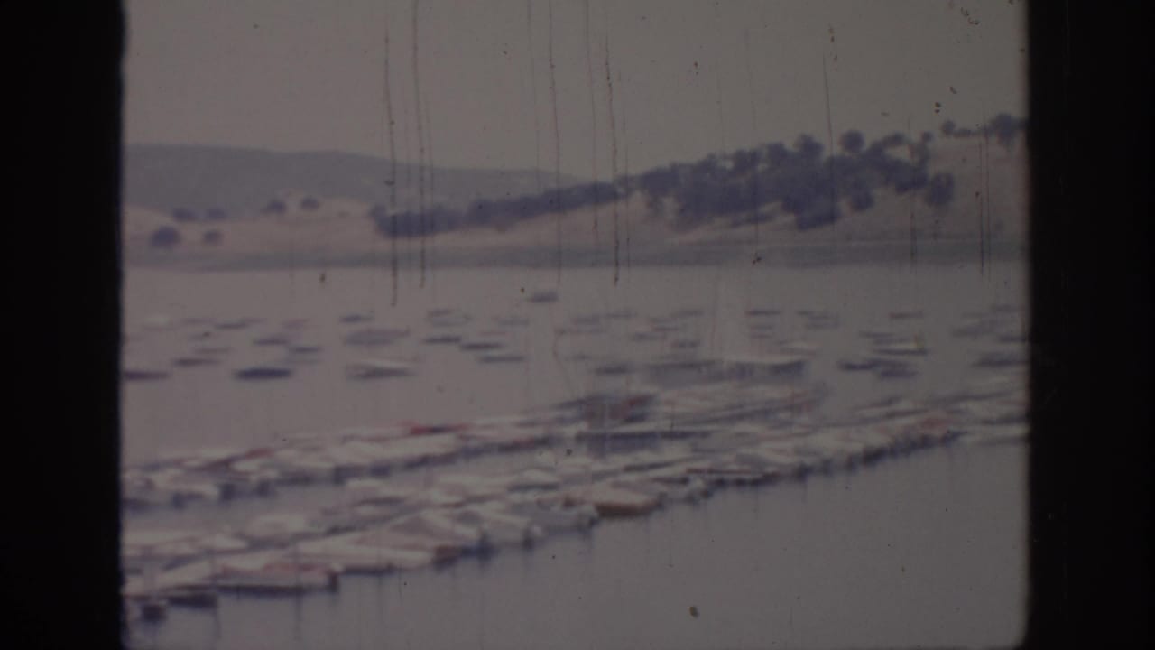 Soft 1966 Sacramento-area 8mm frame showing marina slips, docked boats, still water, and pale hills in the distance.
