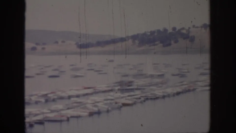 Soft 1966 Sacramento-area 8mm frame showing marina slips, docked boats, still water, and pale hills in the distance.