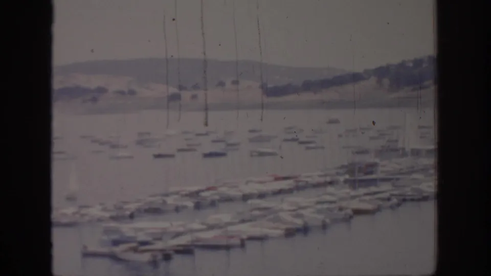 1966 Sacramento-area home-movie frame with docked boats in a marina, still water, distant hills, and vertical window-frame borders.