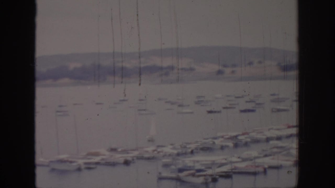 Harbor and marina seen through a vertical window frame, with boats and shoreline hills.