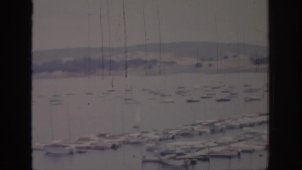 1966 Sacramento waterfront view with a window mullion dividing sailboats, docks, calm water, and distant hills.