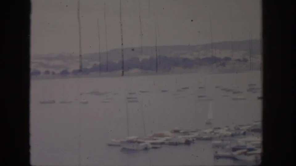 Muted 8mm view of a Sacramento harbor, showing moored boats and a low hillside shoreline through a window.