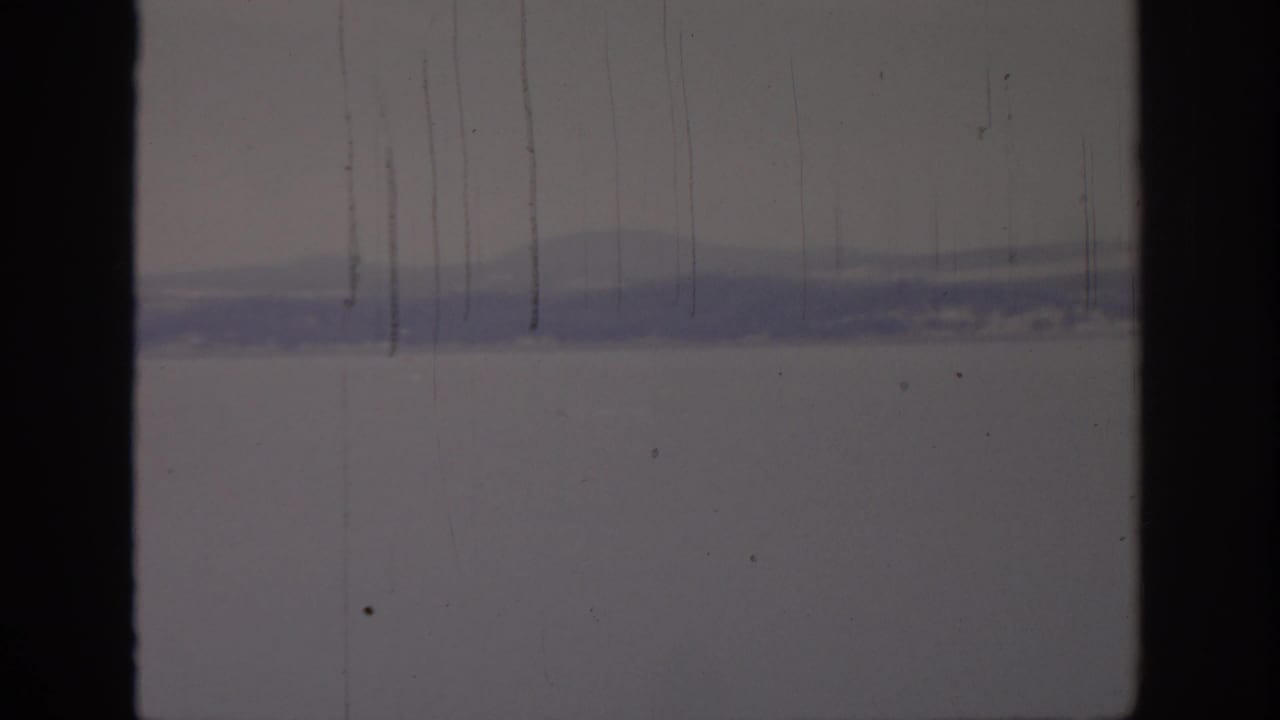 1966 8mm view of a hazy Sacramento-area waterfront, with distant hills and calm water partly obscured by film wear.