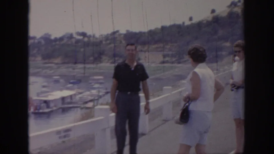 Adult tourists pause on a Sacramento marina pier, with a man facing a woman and another woman partly visible near the railing.
