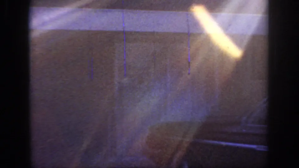 1966 Sacramento home-movie frame with bright flare over a dim residential wall as the camera pans toward the parked sedan.
