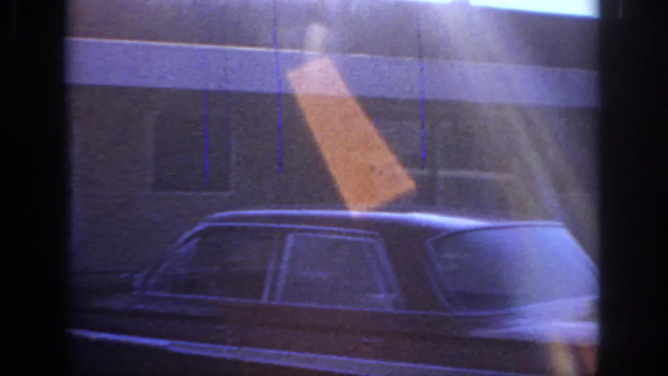 1966 Sacramento frame showing a parked mid-century sedan below a blue-tinted residential facade with flare and grain.