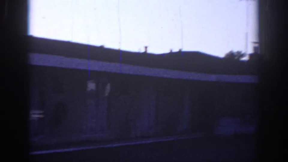 Low-light 1966 Sacramento 8mm view of a single-story building, roofline, parking area, and dark foreground framing.