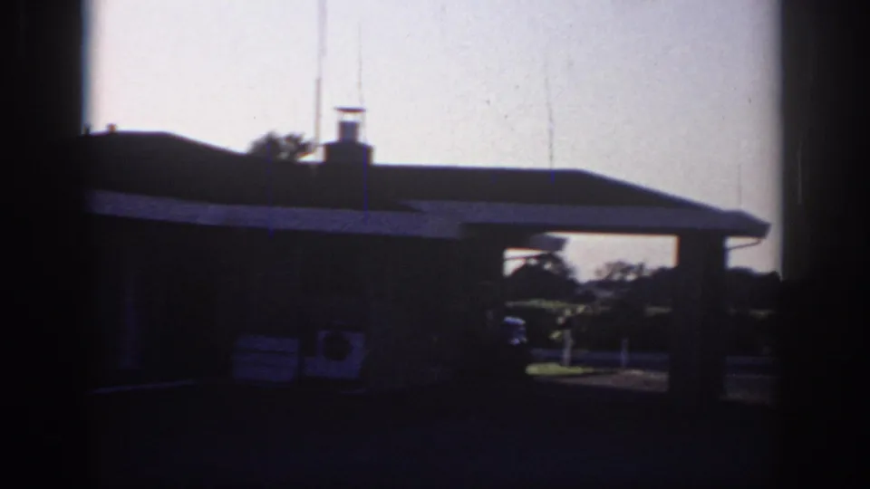 1966 Sacramento frame showing a dark low building, open passage or canopy area, pavement, roofline, and pale dusk sky.