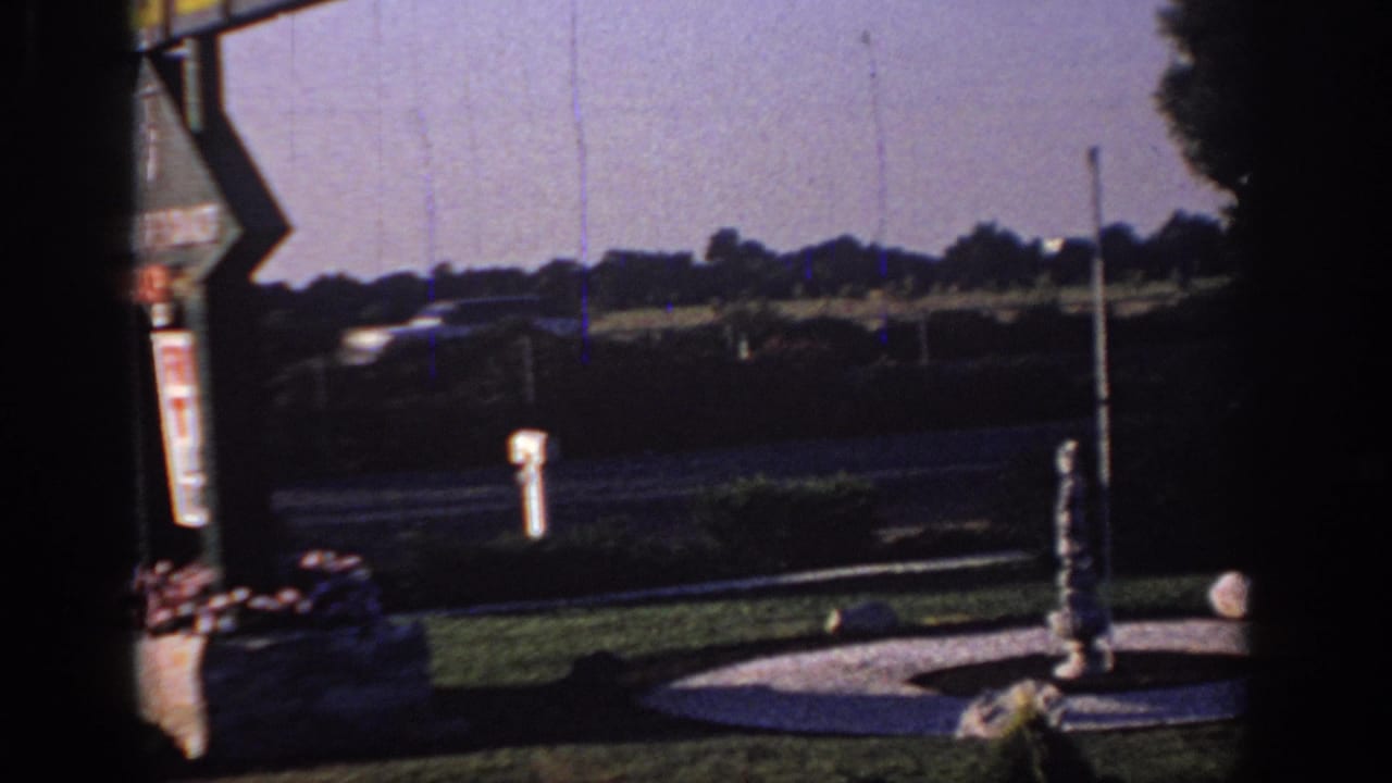 Roadside lawn with signpost and circular fountain area.
