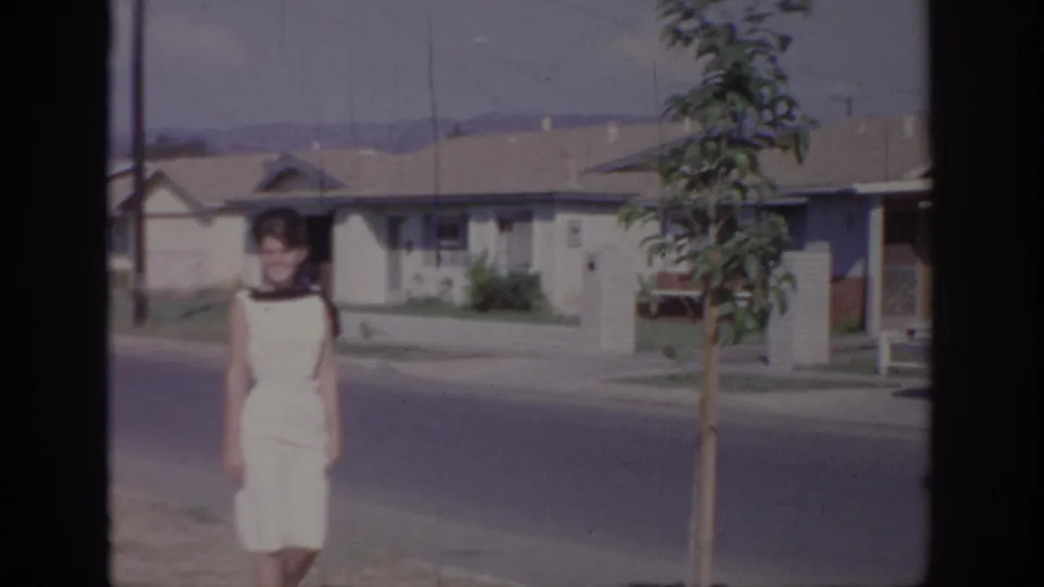 The woman continues along the Sacramento suburban street, with a young sidewalk tree and low ranch homes in view.