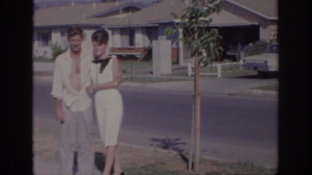 In Sacramento 1966 home-movie footage, a young couple poses on a sidewalk with houses and a parked car behind them.