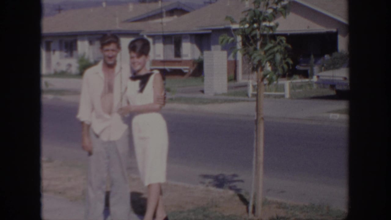 The same couple appears to smile for the camera on a Sacramento residential street, with a driveway and car behind them.