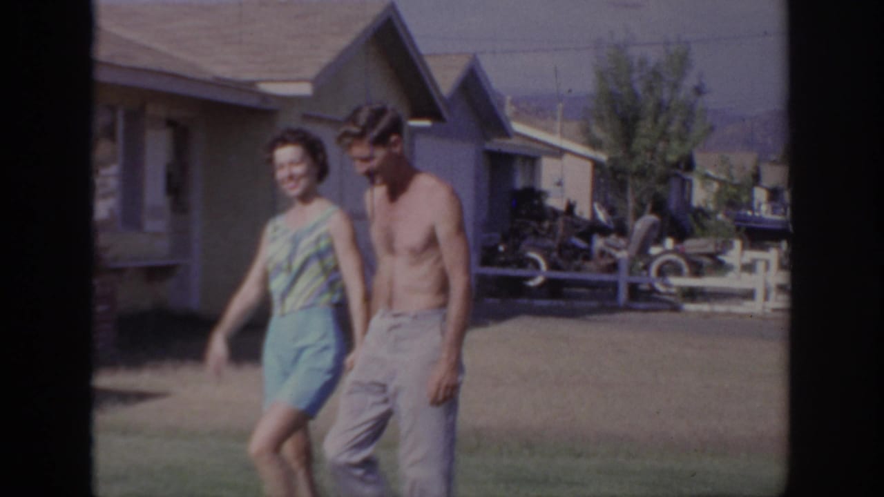 In 1966 Sacramento home-movie footage, a young couple walks together past single-story suburban houses and a lawn.