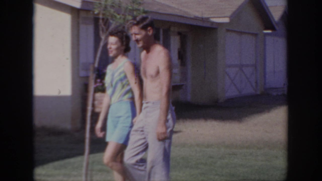 The couple continues walking through a Sacramento suburban yard, framed by a house wall, window, and young tree.