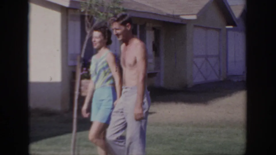 The couple continues walking through a Sacramento suburban yard, framed by a house wall, window, and young tree.
