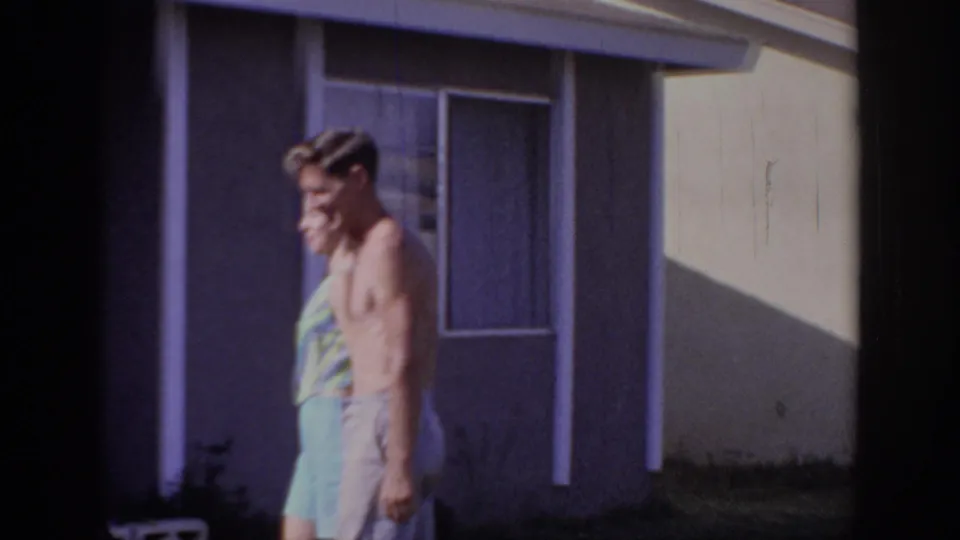 The couple reaches a darker section of the yard near a window and wall of a single-story Sacramento home.