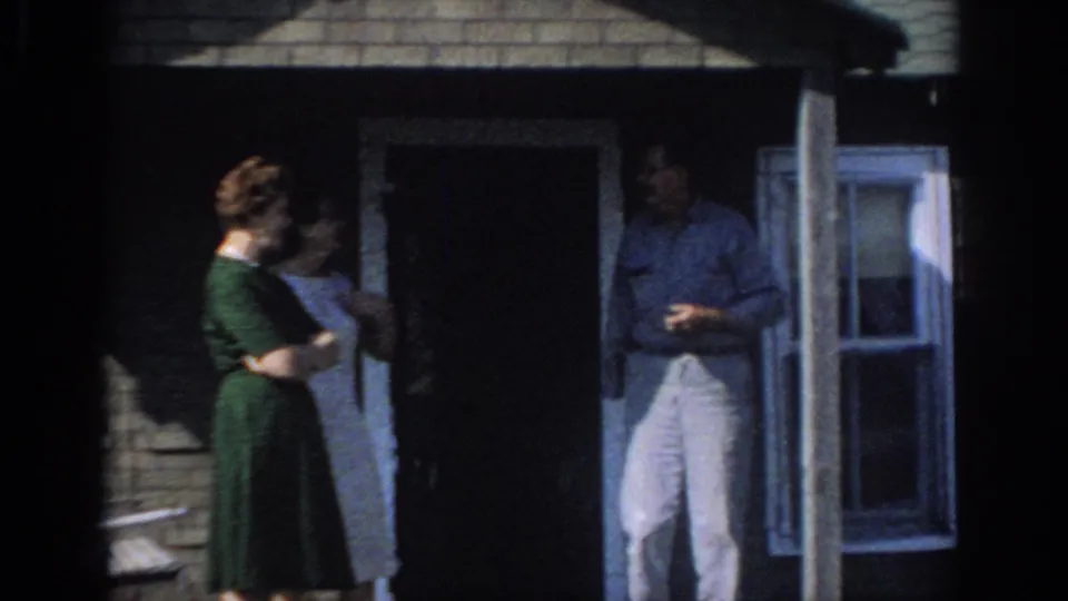 1966 Sacramento home-movie frame of two women and a man standing on a shaded brick house porch.