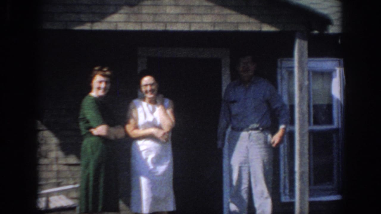 Two women and a man standing outside a brick house.