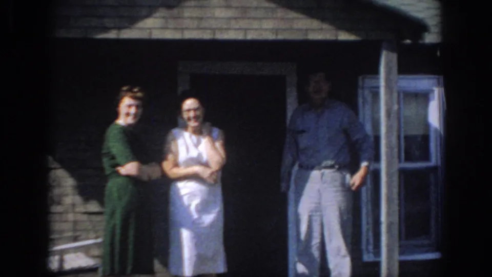 Two women in dresses and a man in light trousers stand outside a Sacramento brick house in 1966 footage.