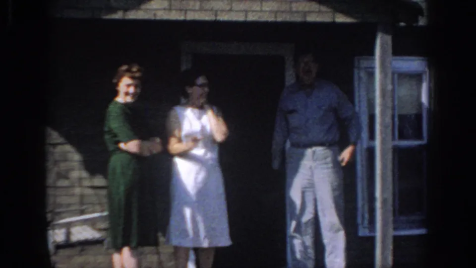 A woman in green, a woman in white, and a man stand by a doorway in 1966 Sacramento home-movie footage.