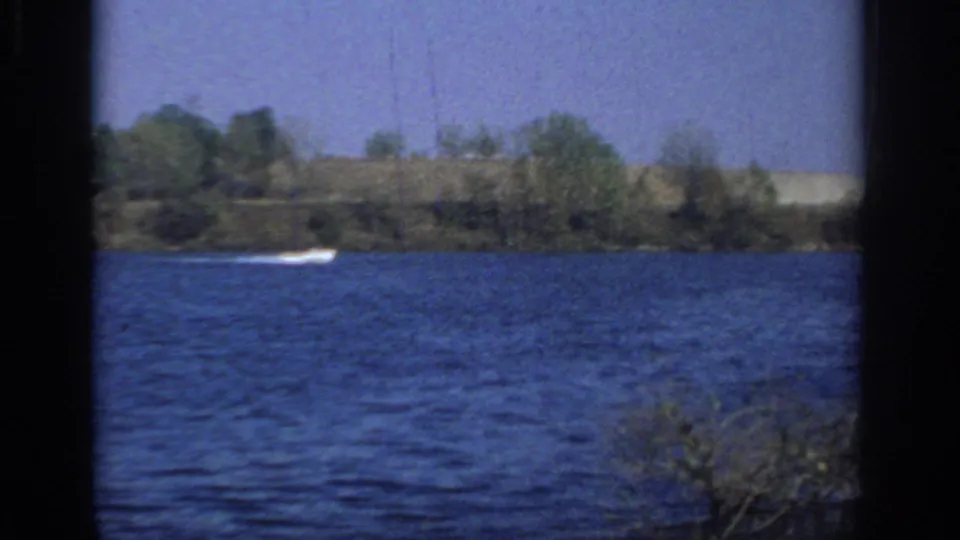 Distant motorboat speeds across blue lake water near Sacramento in a 1966 8mm home-movie scene.