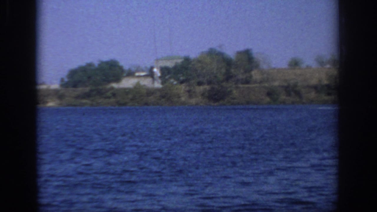 1966 Sacramento-area lake view with rippled water, distant trees, a low building, and dark home-movie frame edges.