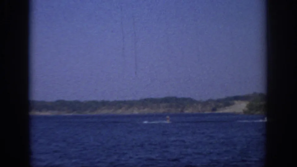 1966 Sacramento-area home-movie frame with open lake water, distant shore, small boating activity, clear sky, and dark 8mm borders.