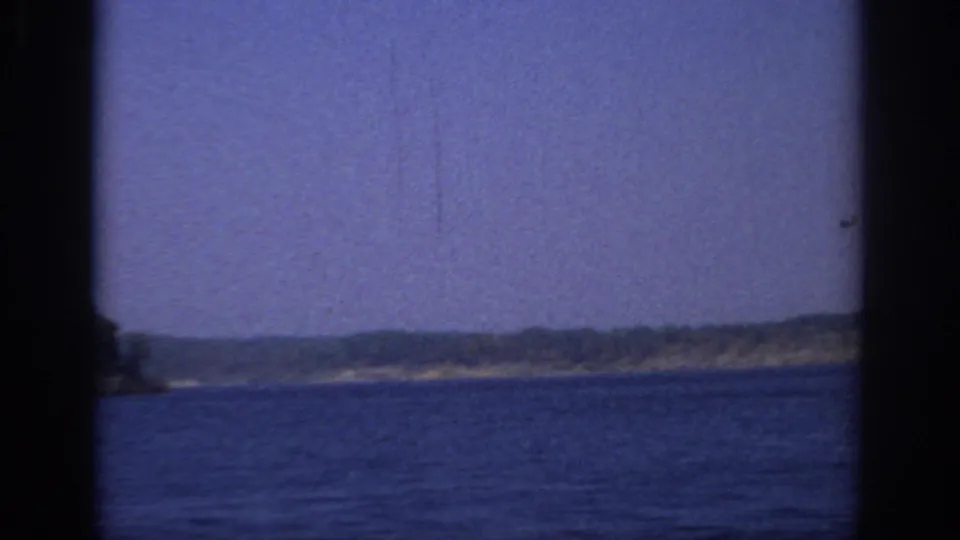 1966 Sacramento-area 8mm frame showing open lake water, a far wooded shoreline, low sandy bank, blue sky, and soft home-movie grain.