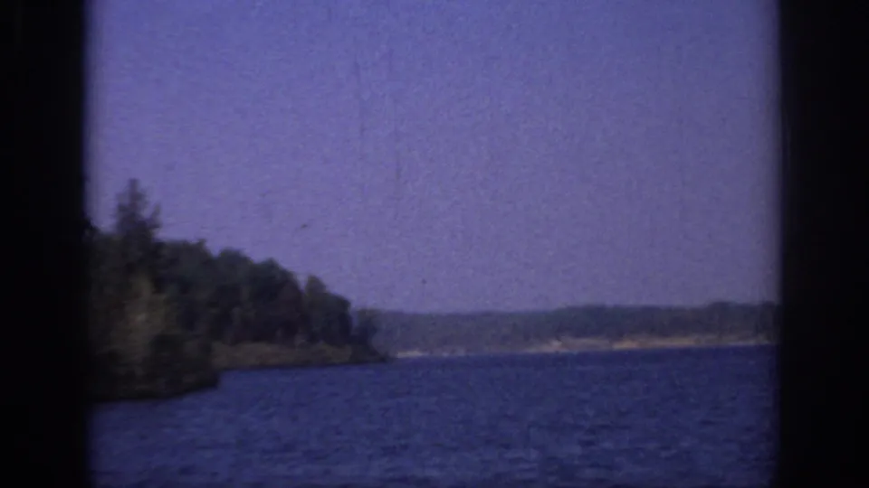 1966 Sacramento-area home-movie frame with a wooded lakeside point, open water, distant shoreline, blue sky, and visible 8mm gate borders.